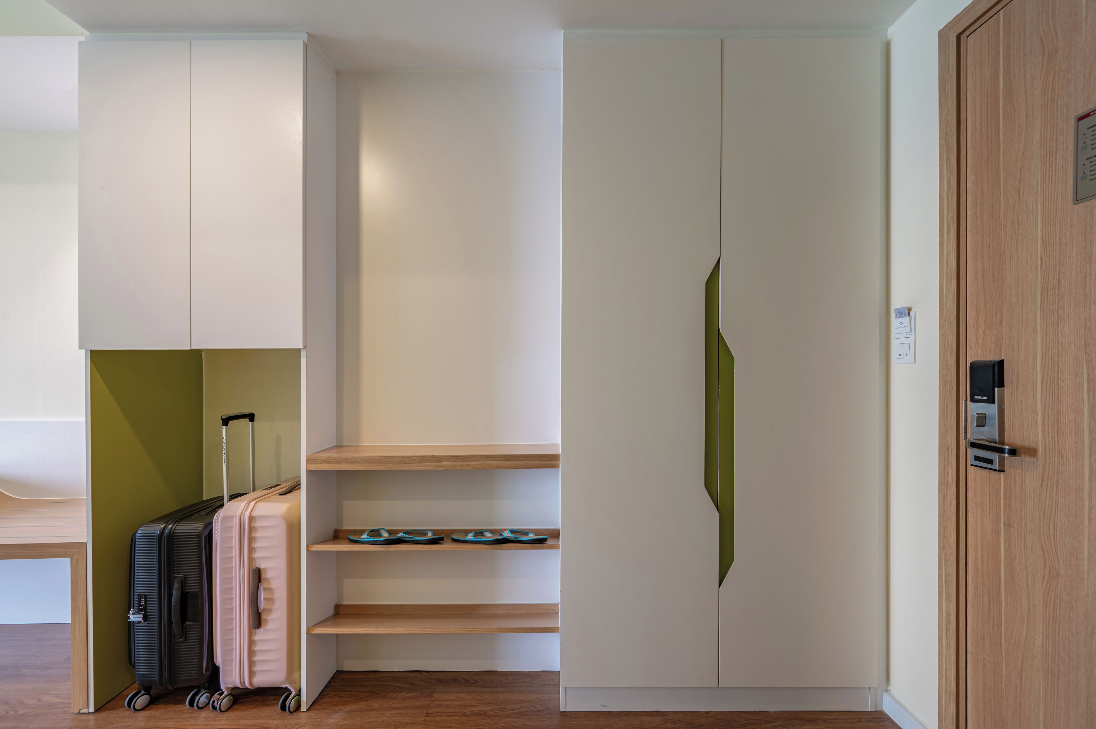 Une chambre d’hôtel avec un plancher en bois, une armoire blanche, un mur vert et une porte dotée d’une poignée.