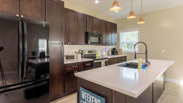 A modern kitchen with dark wood cabinets, stainless steel appliances, and a large island with a sign reading "Weekend Forecast".
