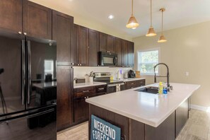 Una cocina moderna con armarios de madera oscura, electrodomésticos de acero inoxidable y una isla grande con un cartel que dice 'Pronóstico del fin de semana'.