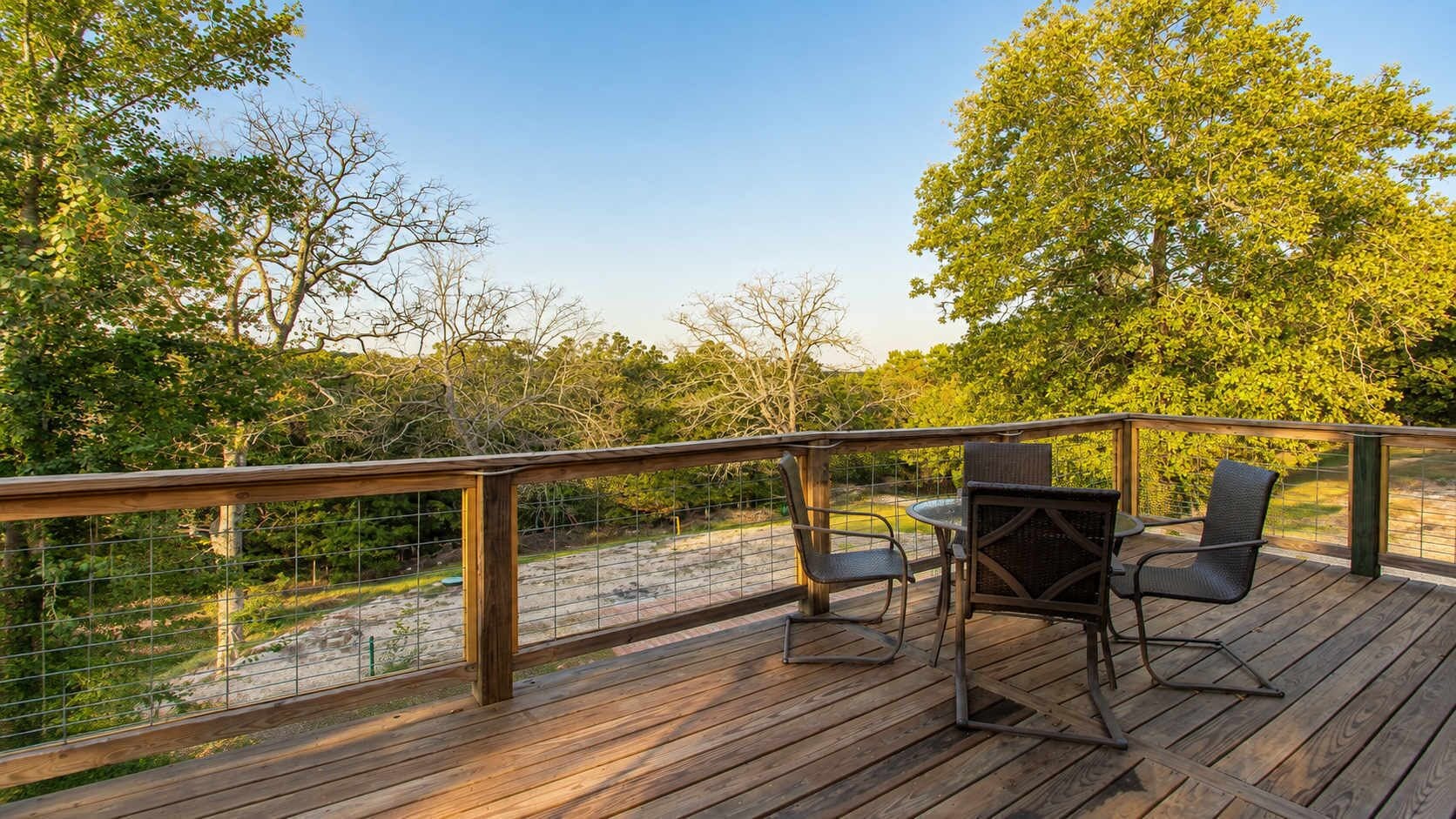 Une terrasse en bois avec une rambarde en métal, deux chaises en osier et une table.
