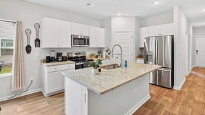 A modern kitchen with white cabinetry, a granite countertop, stainless steel appliances, and a small island.