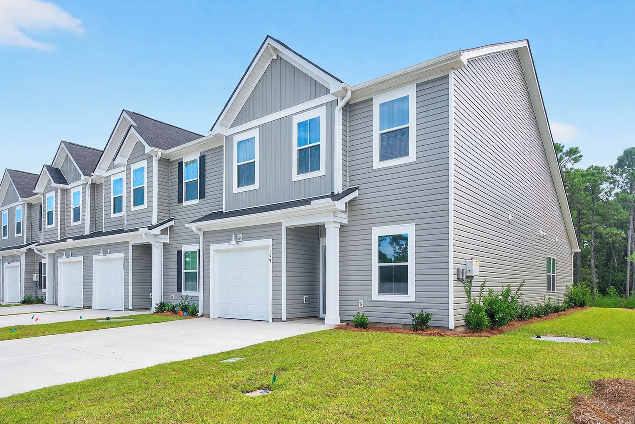 A row of modern townhouses with grey siding and white trim, featuring multiple garage doors and a well-maintained lawn.