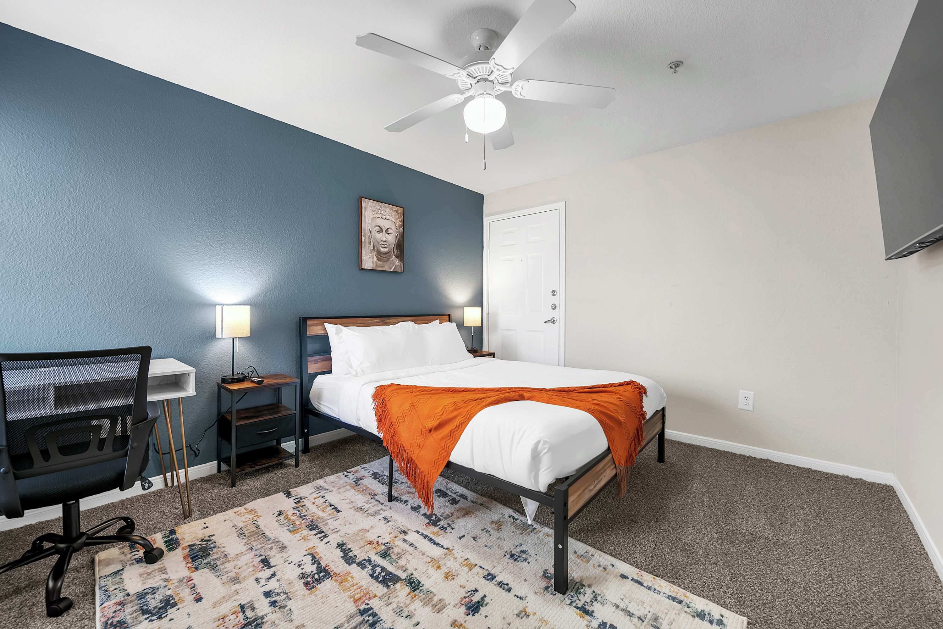 A bedroom with a bed, desk, chair, and a ceiling fan.