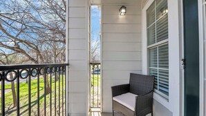 A balcony with a wicker chair, a view of trees, and a building in the background. - Apartment w/pool & hot tub + gym (Austin)