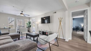 A modern living room with a sofa set, a coffee table, a TV, and a desk area. - Apartment w/pool & hot tub + gym (Austin)