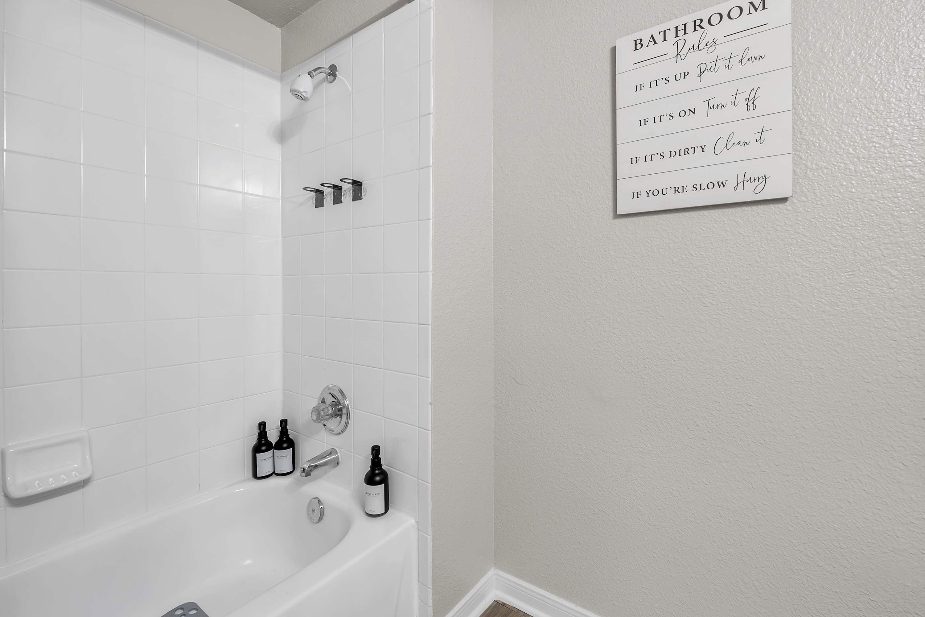 A bathroom with white tiles, a bathtub, and a wall-mounted sign listing bathroom rules.