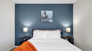 A hotel room with a bed, two bedside tables with lamps, a wall-mounted picture, and an orange throw blanket. - Apartment w/pool & hot tub + gym (Austin)