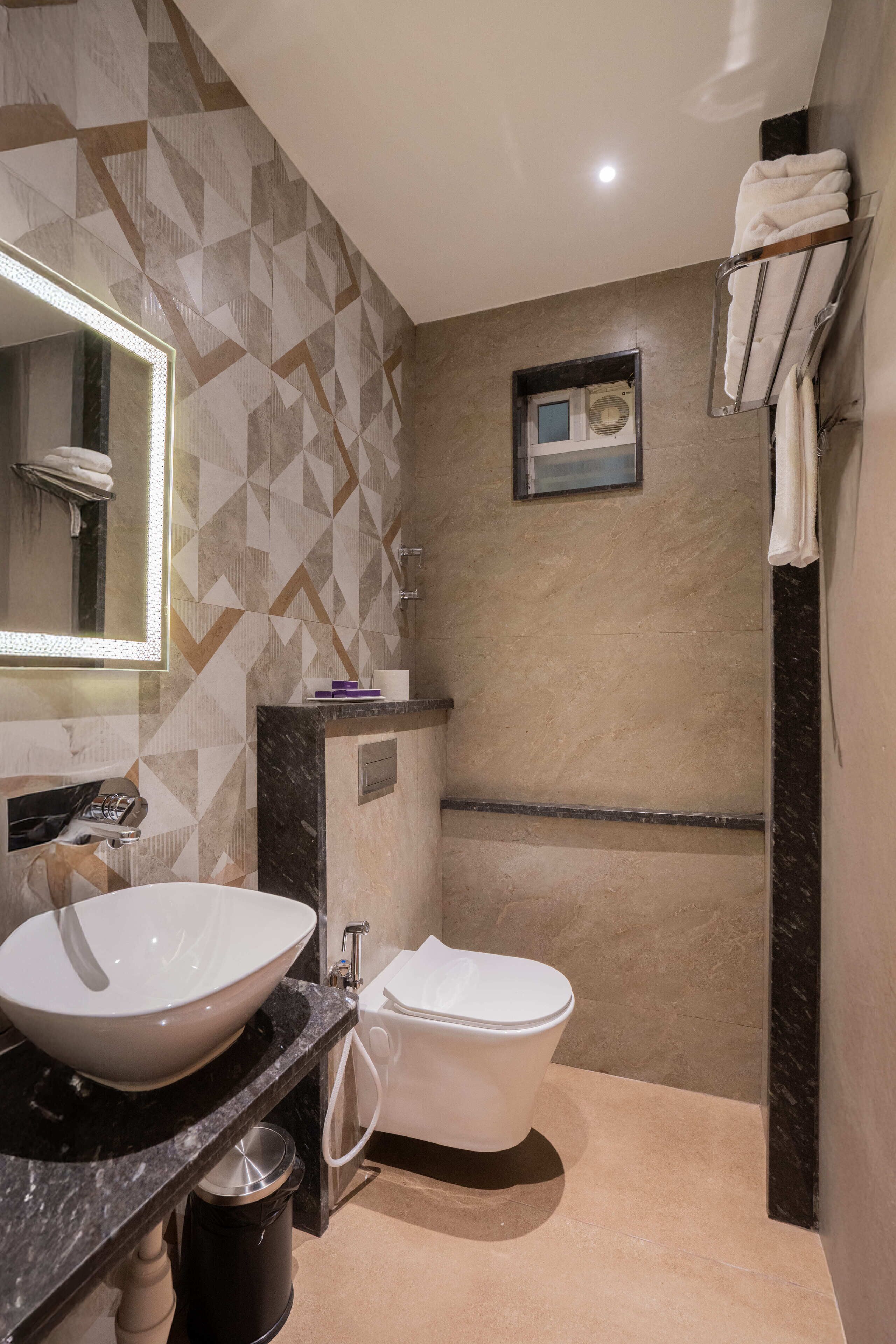 A modern bathroom with a large mirror, a white sink, a toilet, and a towel rack.