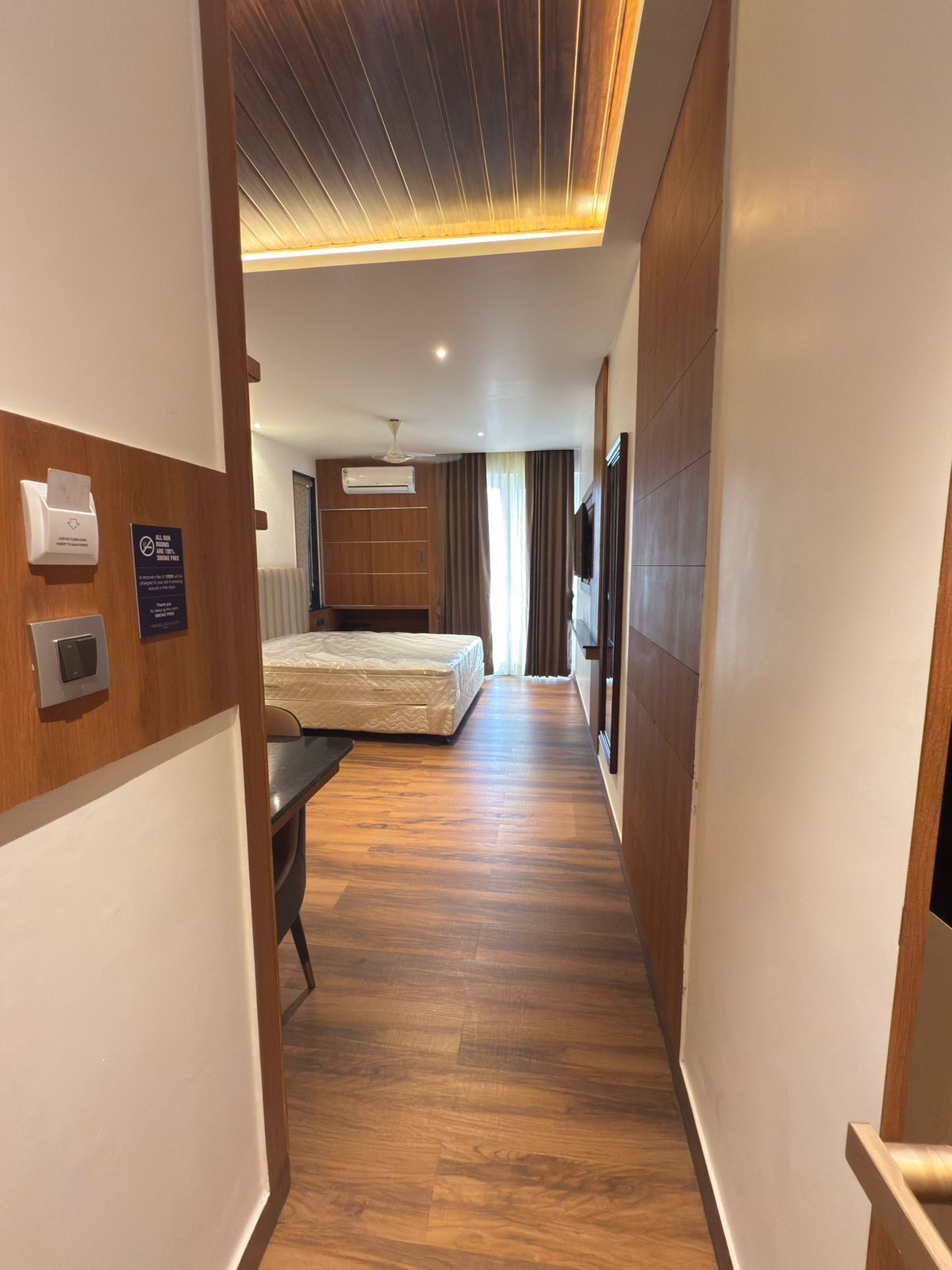 A hotel hallway with a wooden floor, a bed, a desk, and a TV.