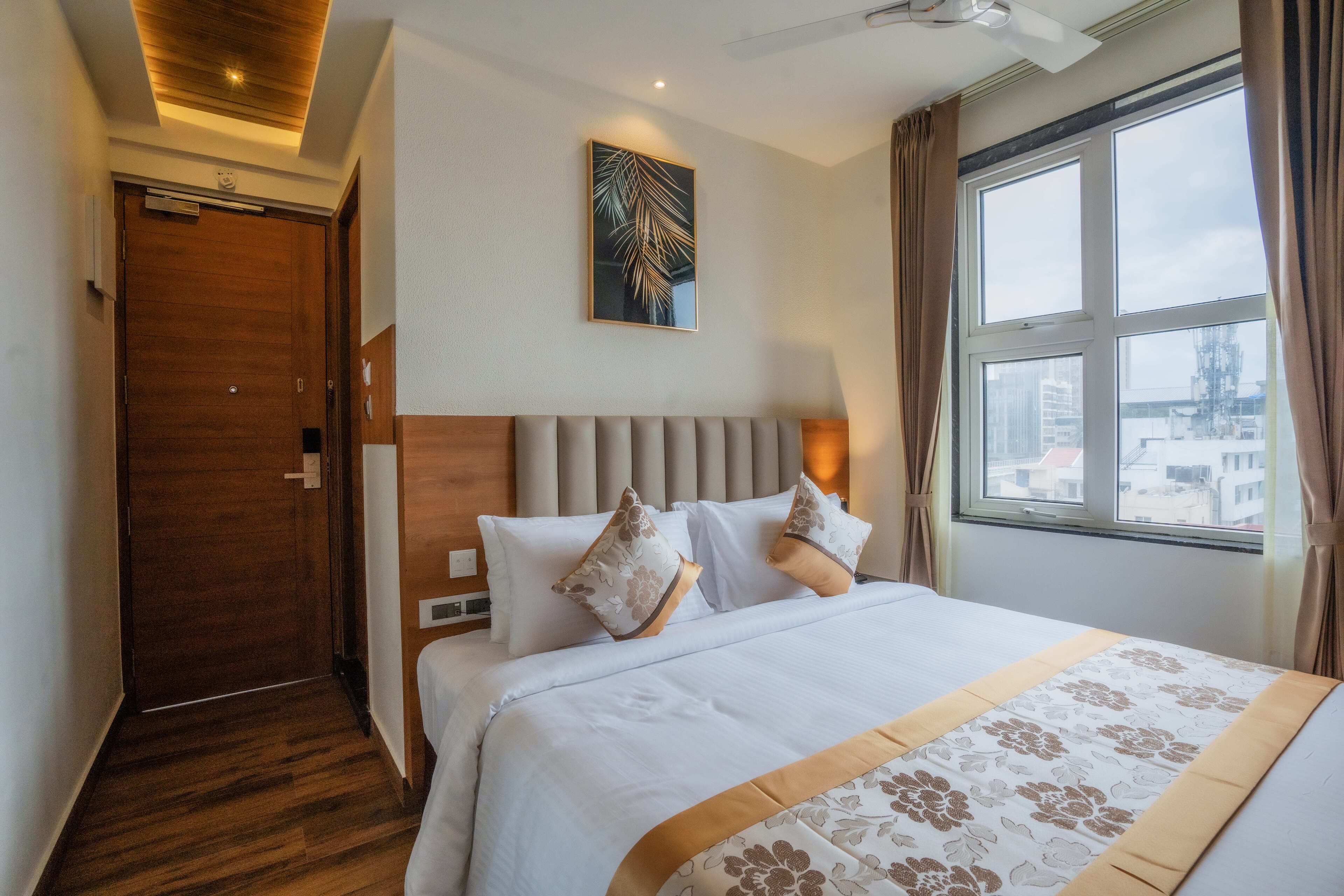 Una habitación de hotel con una cama grande, cabecera, ventana con cortinas y ventilador de techo.