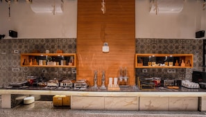 A kitchen area with a marble countertop, two wooden shelves with kitchenware, and a central wooden panel.