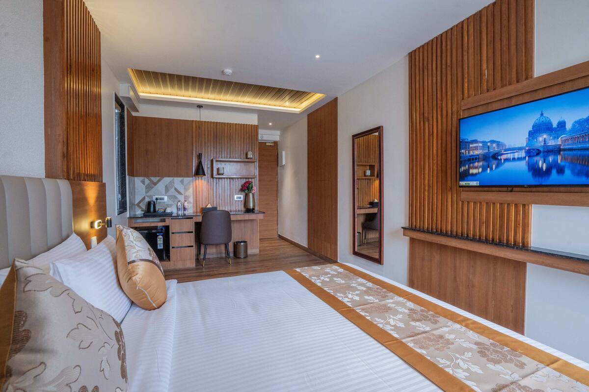 A hotel room with a large bed, a desk, a television, and a view of a cityscape.