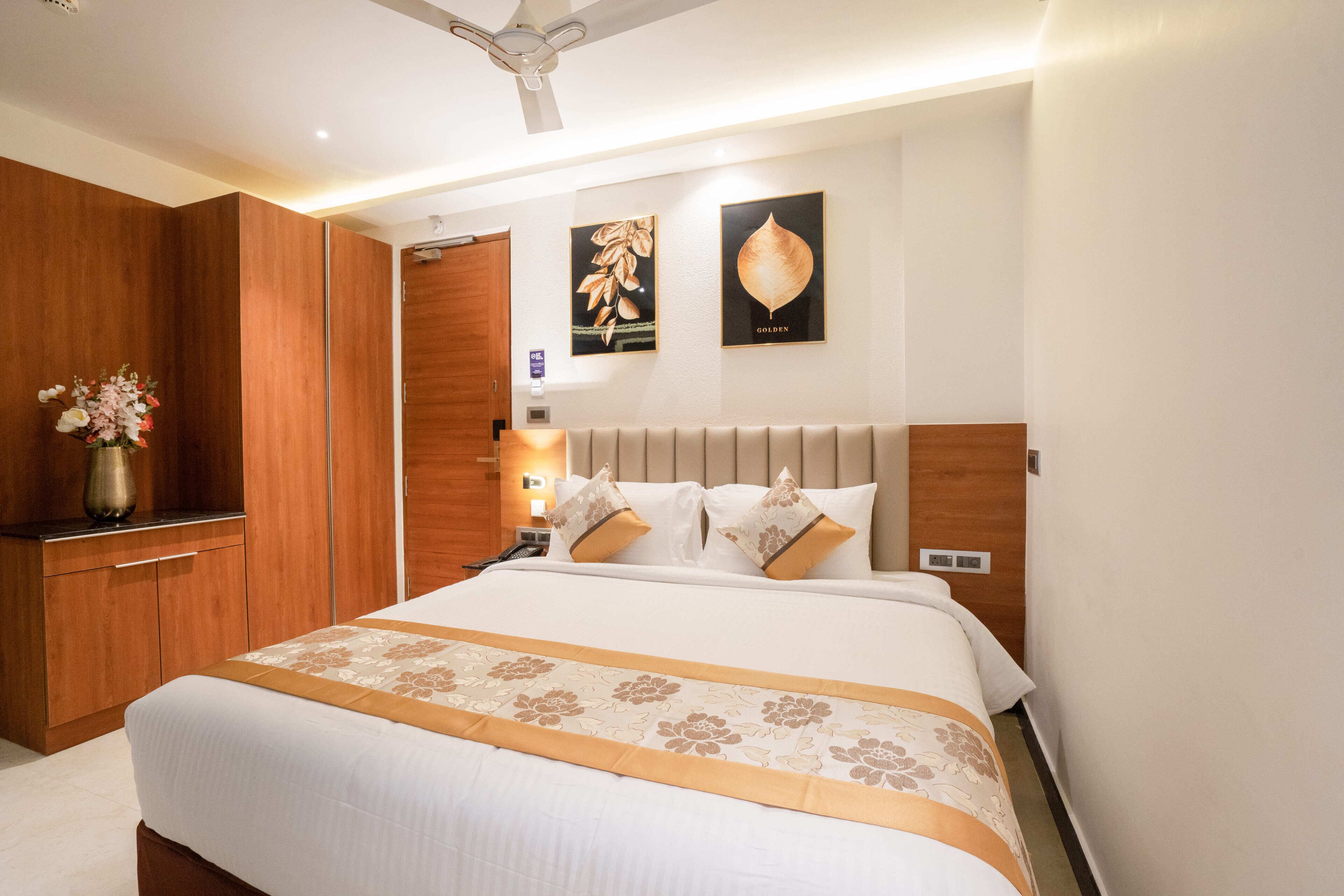 A well-lit hotel room with a large bed, wooden wardrobe, and a ceiling fan.