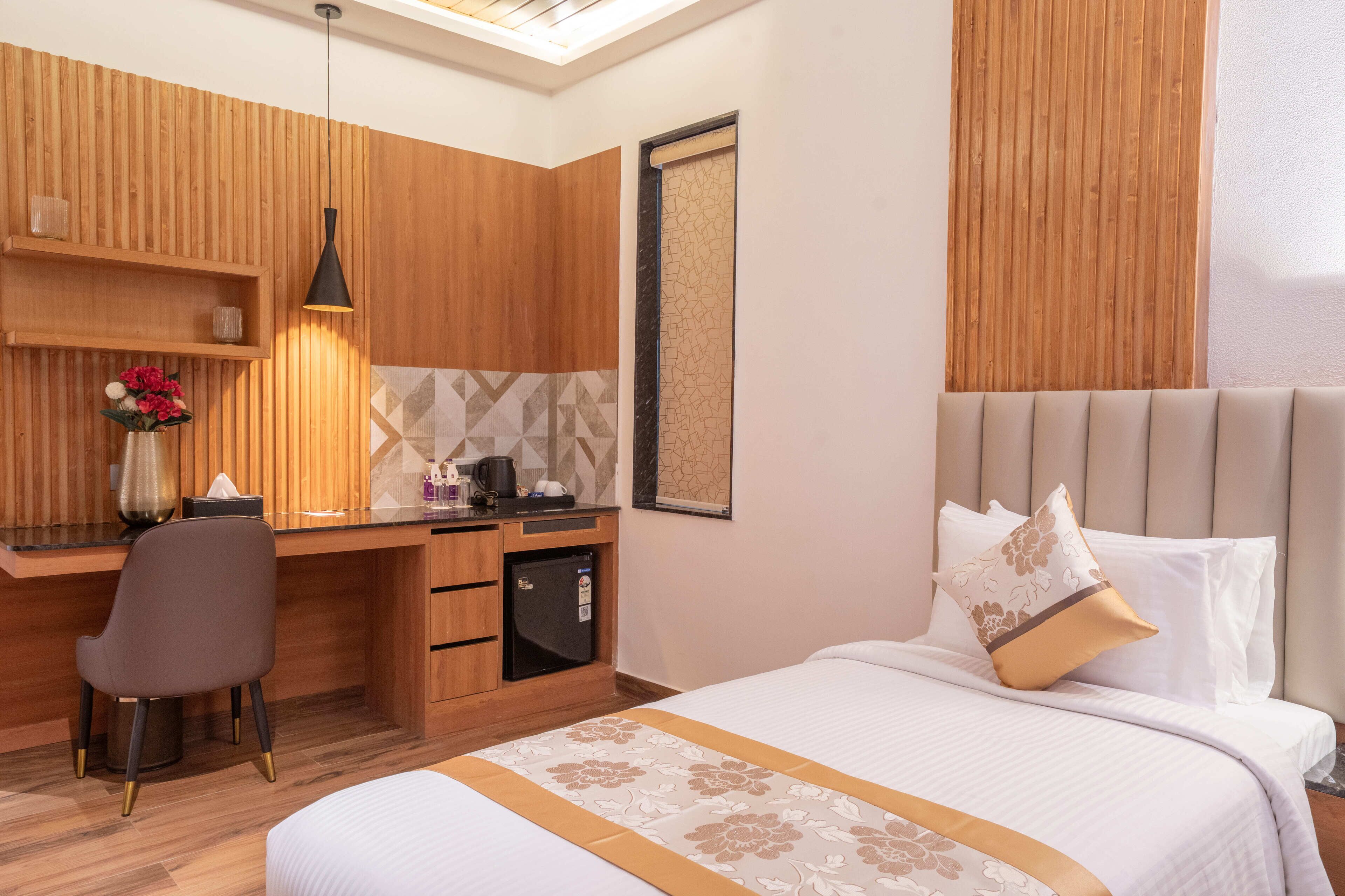 Una habitación de hotel con un escritorio de madera, una cama con colcha estampada y un refrigerador pequeño.