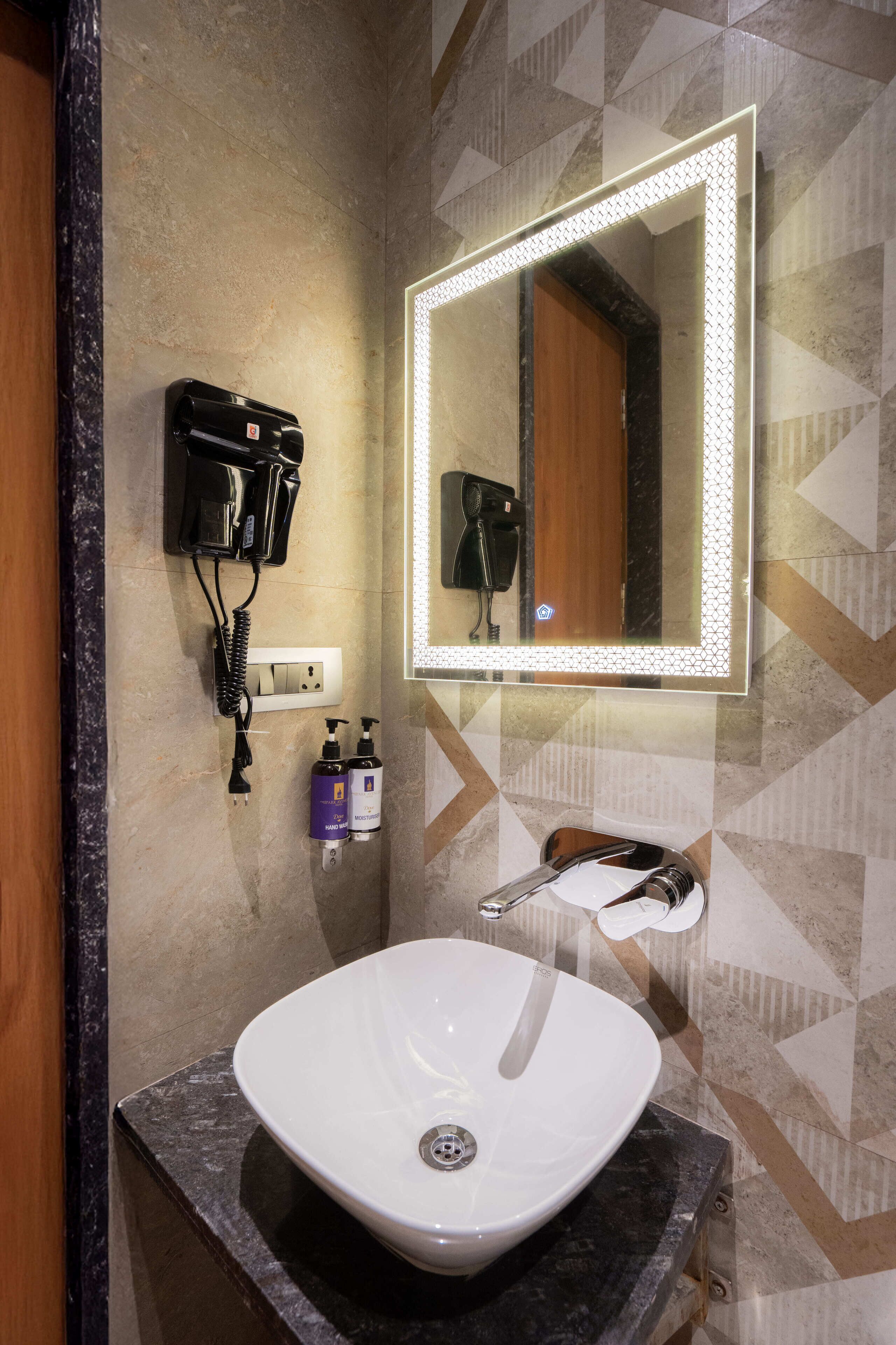 A bathroom with a white sink, a mirror with LED lights, a hairdryer, and two bottles of shampoo.