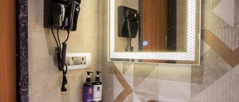 A bathroom with a white sink, a mirror with LED lights, a hairdryer, and two bottles of shampoo.