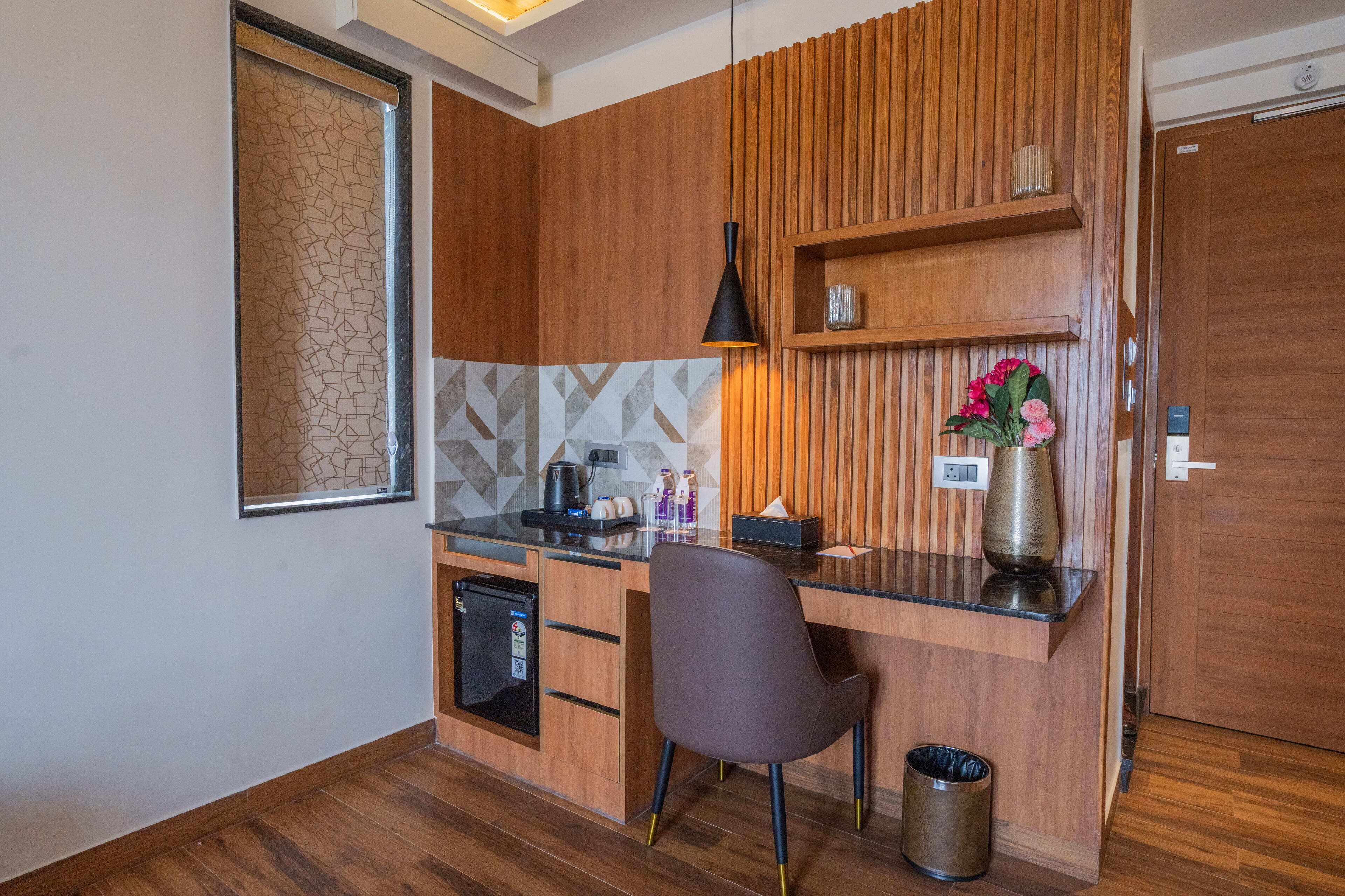 Een kleine keuken met houten kastjes, een inbouwkoelkast, een zwart aanrecht, een moderne hanglamp en een vaas met bloemen.