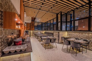 Un restaurante con techo de madera, paredes enlosadas y una zona de bar. Mesas y sillas dispuestas para comer.