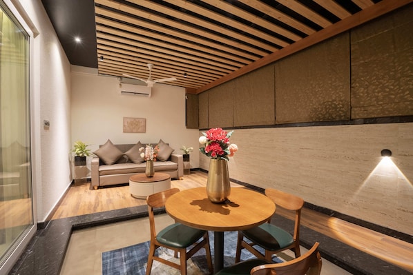 A modern living room with a round wooden table, green cushioned chairs, a beige sofa, and a vase of flowers.