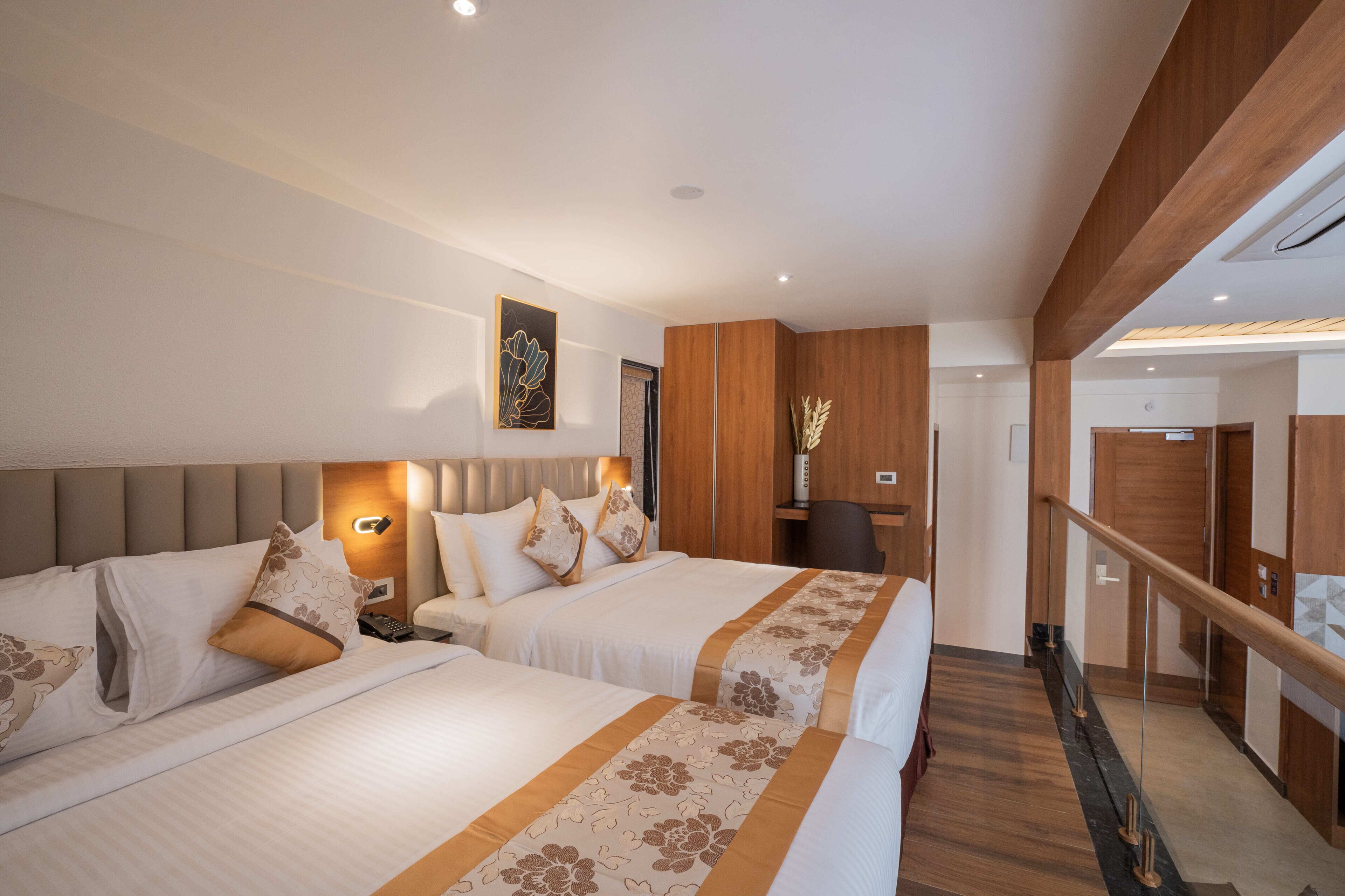 A hotel room with two beds, a wooden ceiling, a desk, and a staircase.