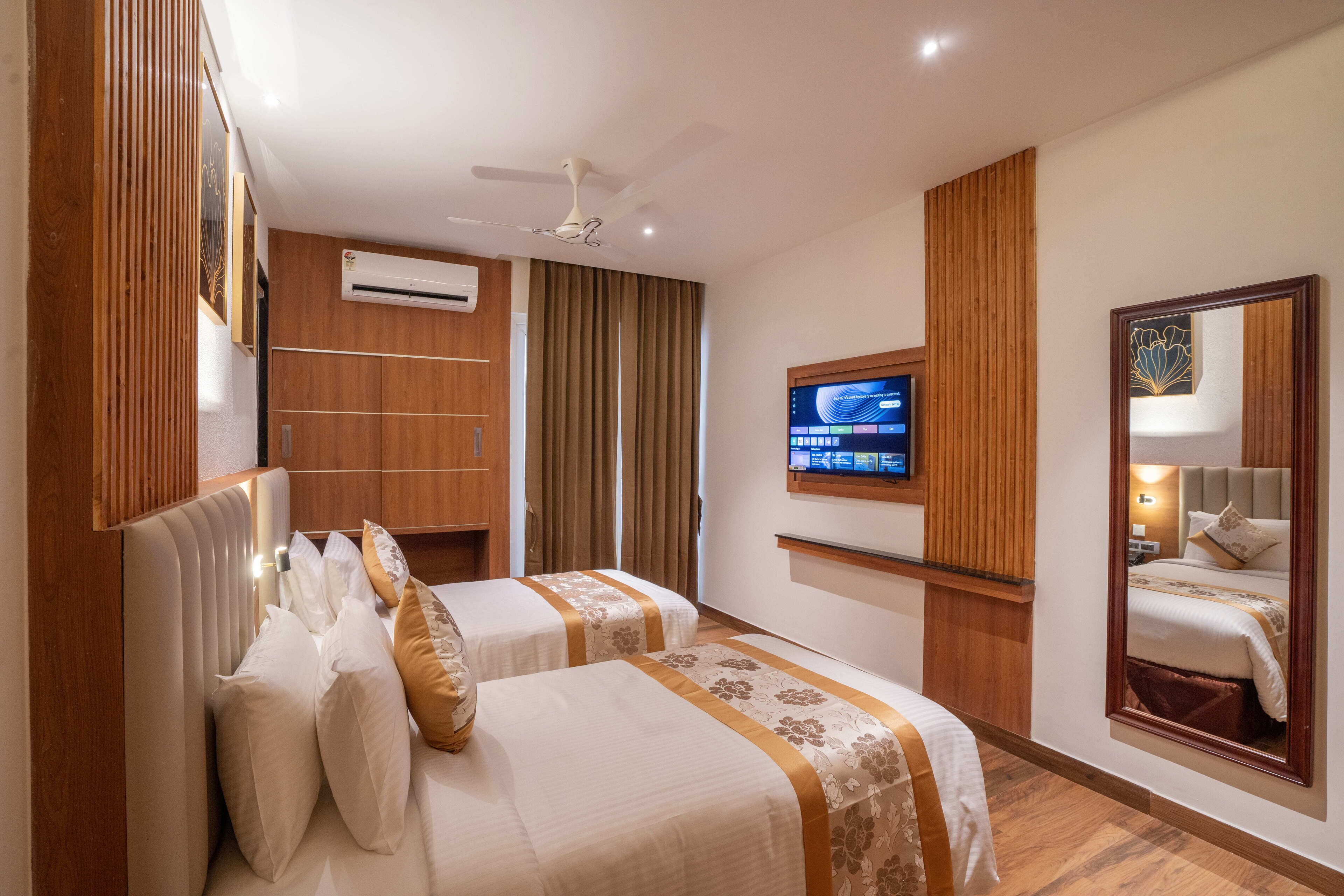 Ein Hotelzimmer mit zwei Betten, einem Fernseher, einer Klimaanlage und einem Deckenventilator.