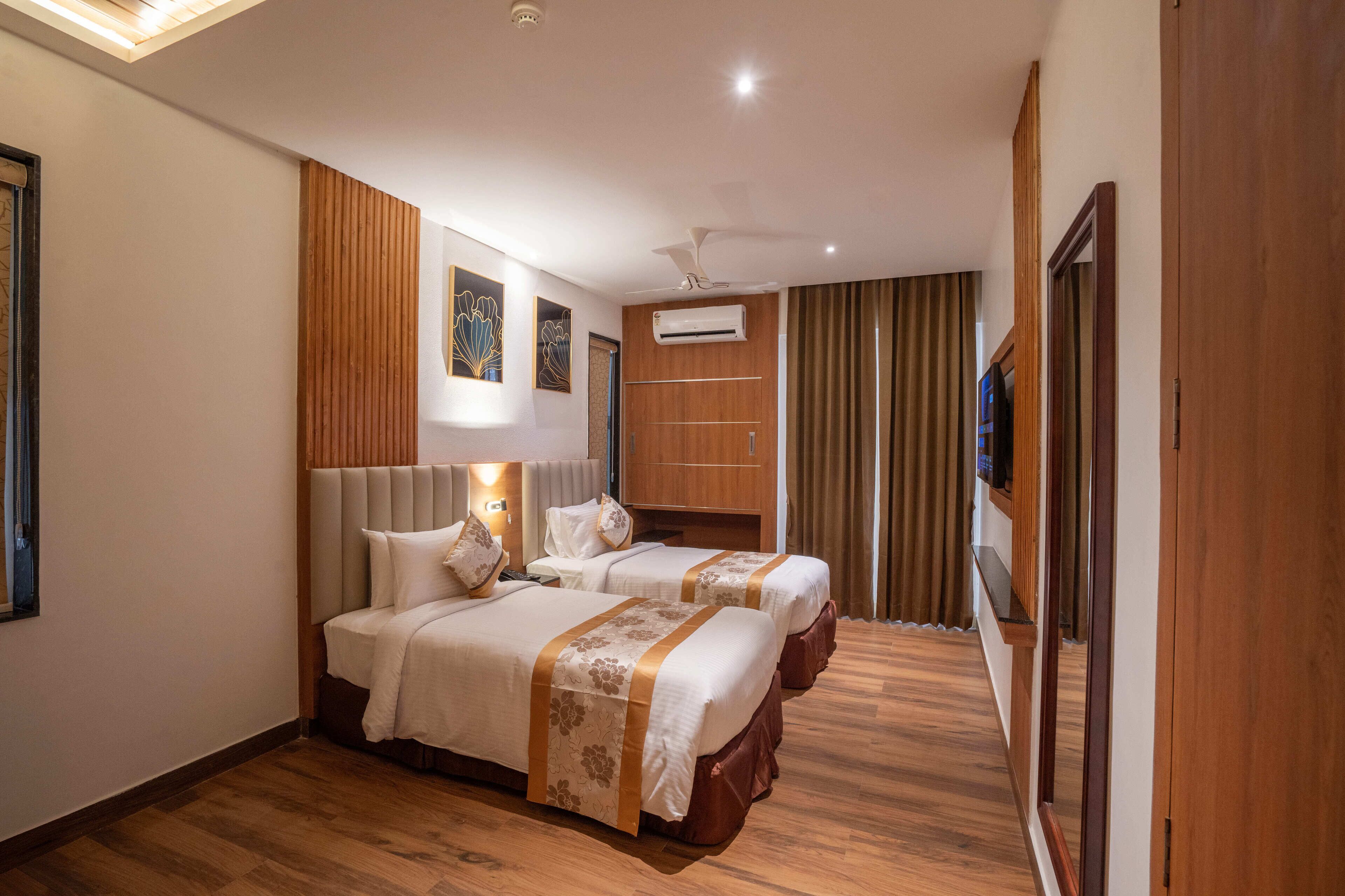 A hotel room with two beds, a ceiling fan, an air conditioning unit, wooden paneling, and a TV on the wall.