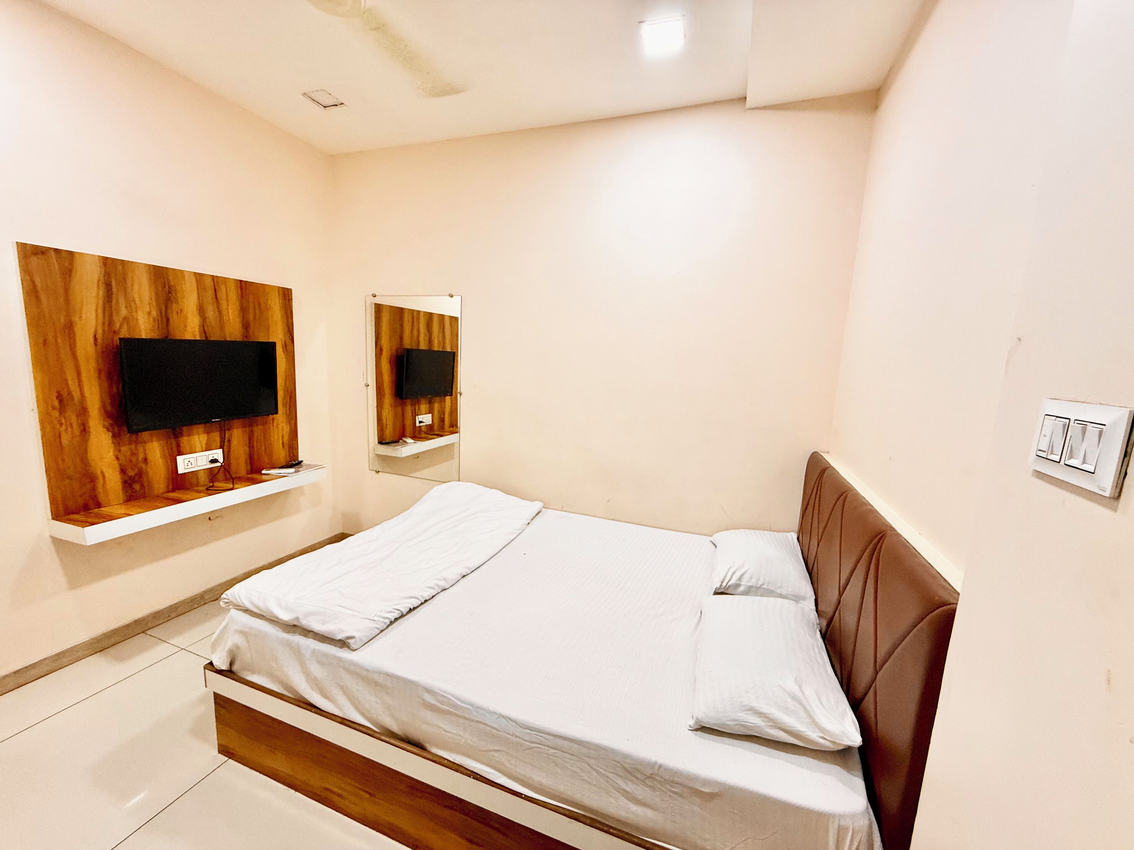 Een slaapkamer met een bed, een aan een houten paneel bevestigde televisie en een spiegel.