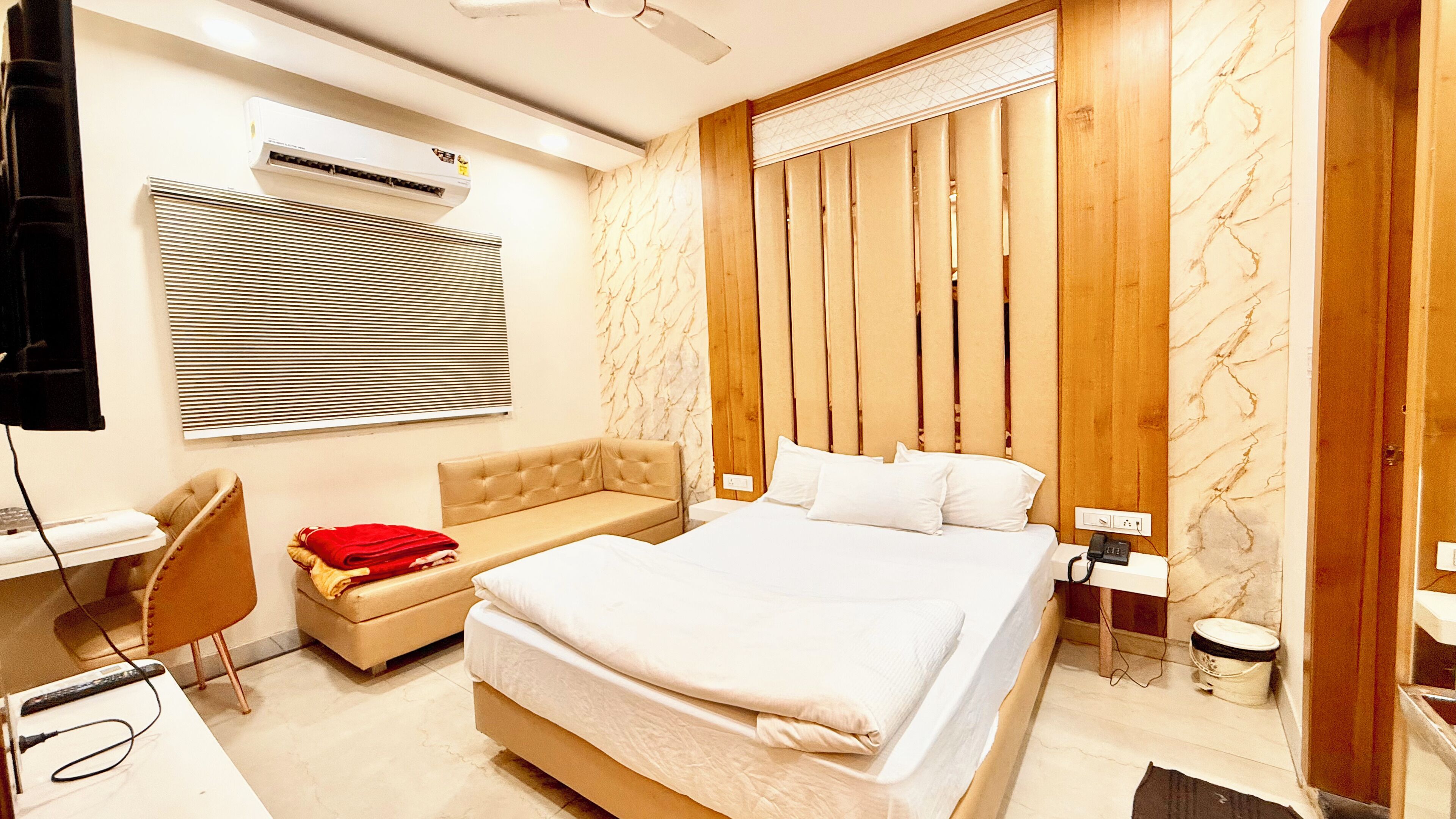 A hotel room with a bed, a desk, a chair, a TV, and a window with blinds.
