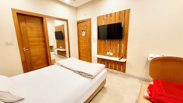 Habitación de hotel con una cama, un televisor montado en la pared, una puerta de madera y un pequeño estante.