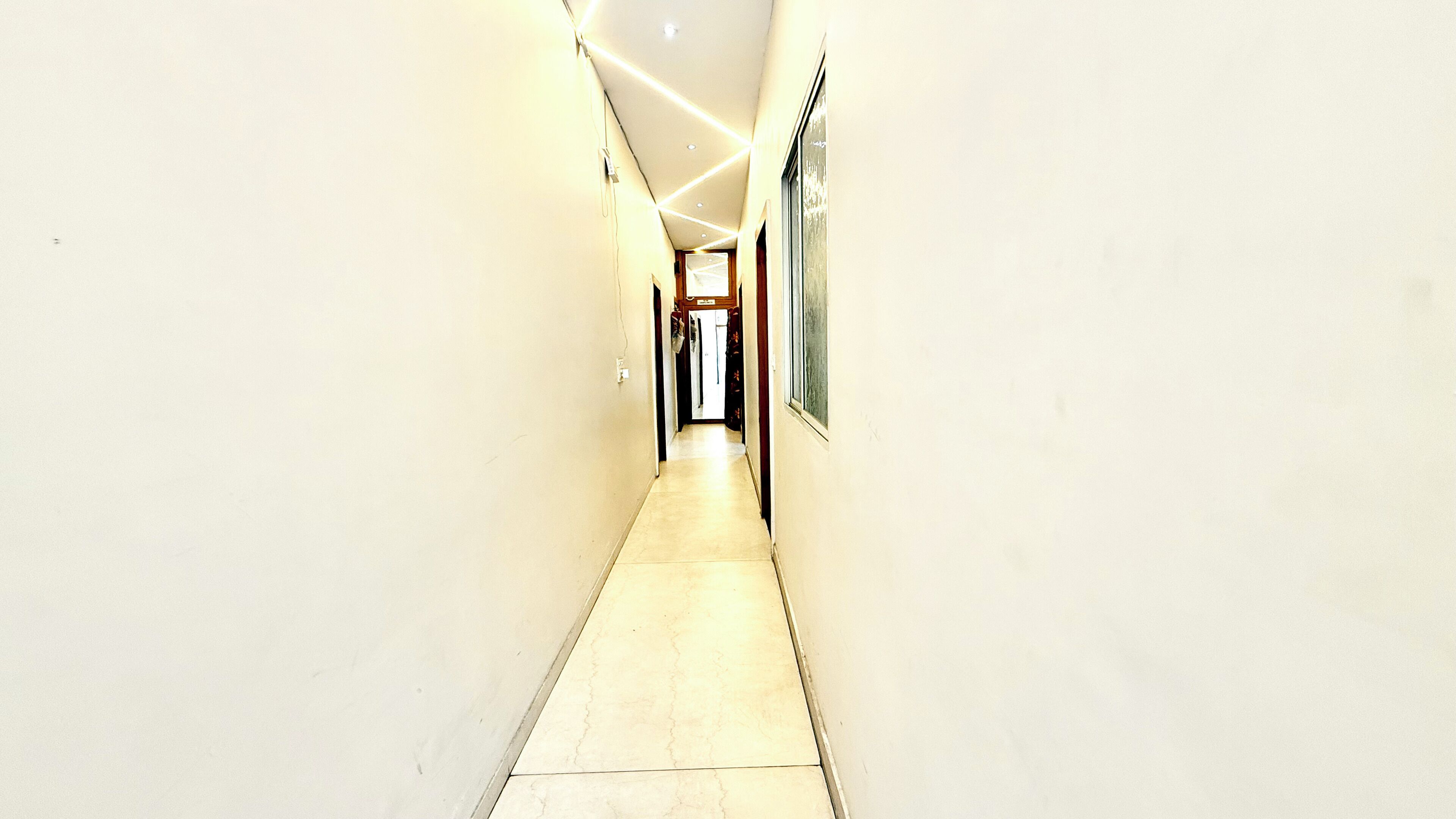 A narrow, well-lit hallway with a tiled floor, leading to a door at the end.