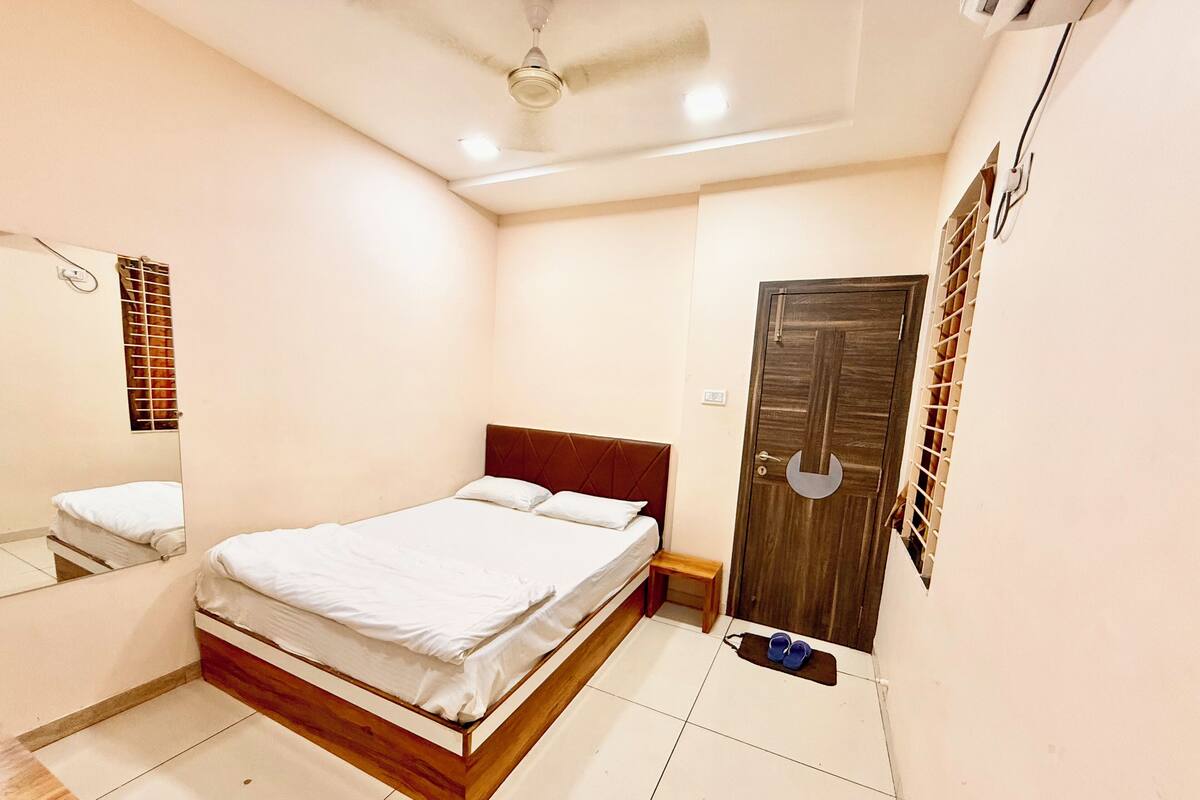 Une chambre à coucher avec un lit, une tête de lit en bois, un miroir, une porte et un ventilateur de plafond.