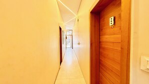 Un pasillo largo y estrecho con puertas de madera en un lado y una pared blanca en el otro.