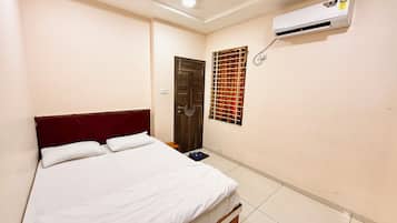 A bedroom with a bed, a ceiling fan, an air conditioning unit, a window with a metal grill, and a door.