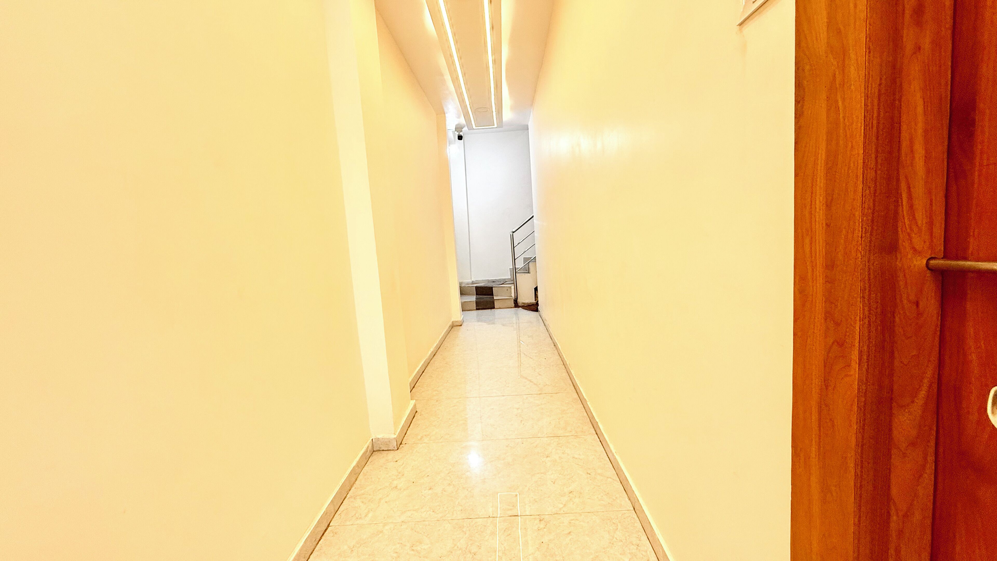 Un pasillo estrecho con una puerta de madera a la derecha y una escalera al final.