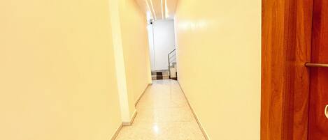 Un pasillo estrecho con una puerta de madera a la derecha y una escalera al final.