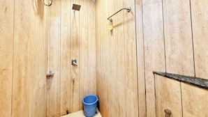 Un baño con paneles de madera, una ducha, un inodoro y un cubo azul.
