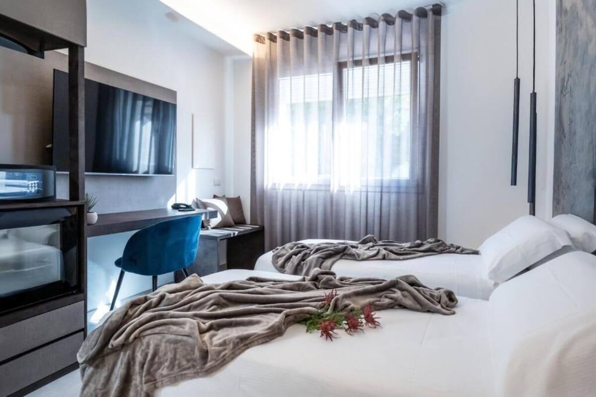 A hotel room with two beds, a desk, a chair, and a TV.