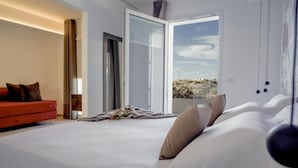 A modern hotel room with a large bed, a red sofa, and a balcony with a view. - Alba in Cento (Lampedusa)