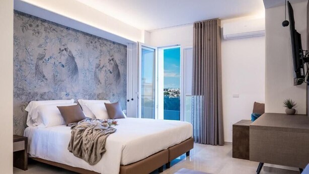A modern bedroom with a large bed, a desk, and a view of the city. - Alba in Cento (Lampedusa)