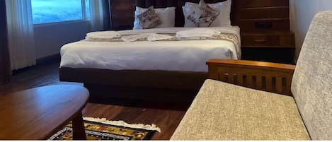 A hotel room with a large bed, two wall-mounted lights, a wooden headboard, a window with curtains, and a small table with a magazine.