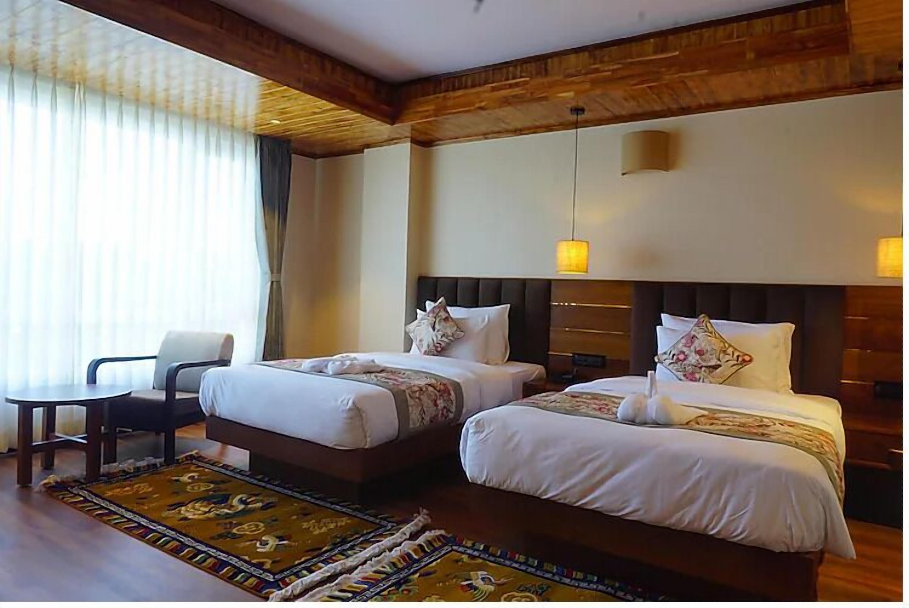 Habitación de hotel con dos camas, techo de madera, una mesita y una silla.