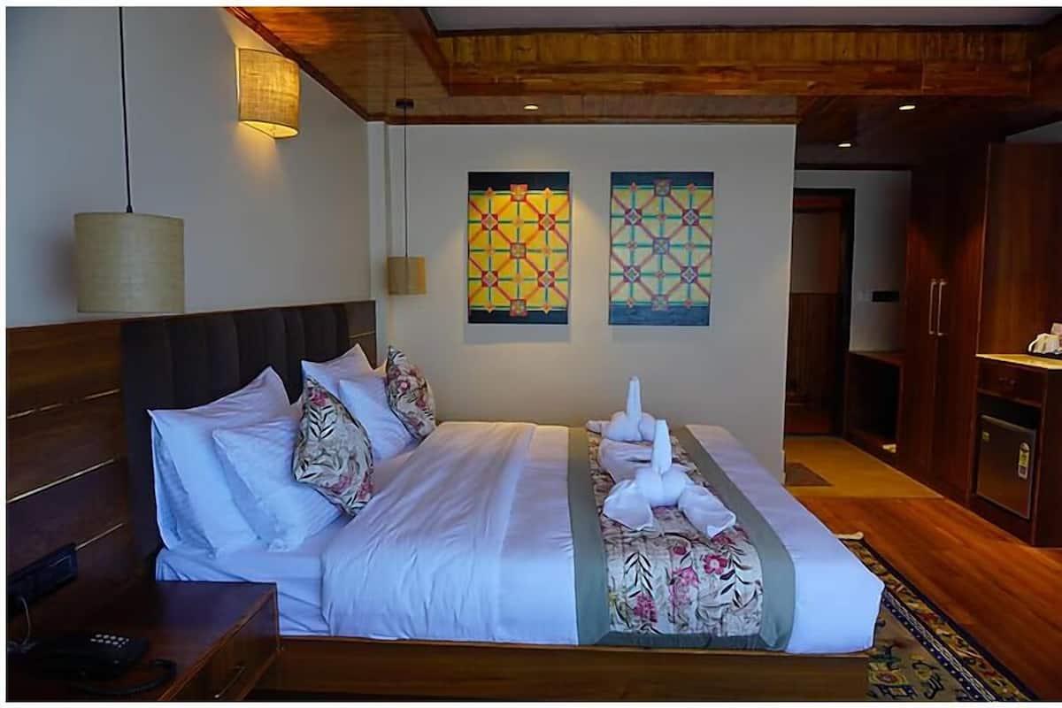 Habitación de hotel con una cama grande, cabecero de madera, dos lámparas fijadas a la pared y dos obras de arte enmarcadas.