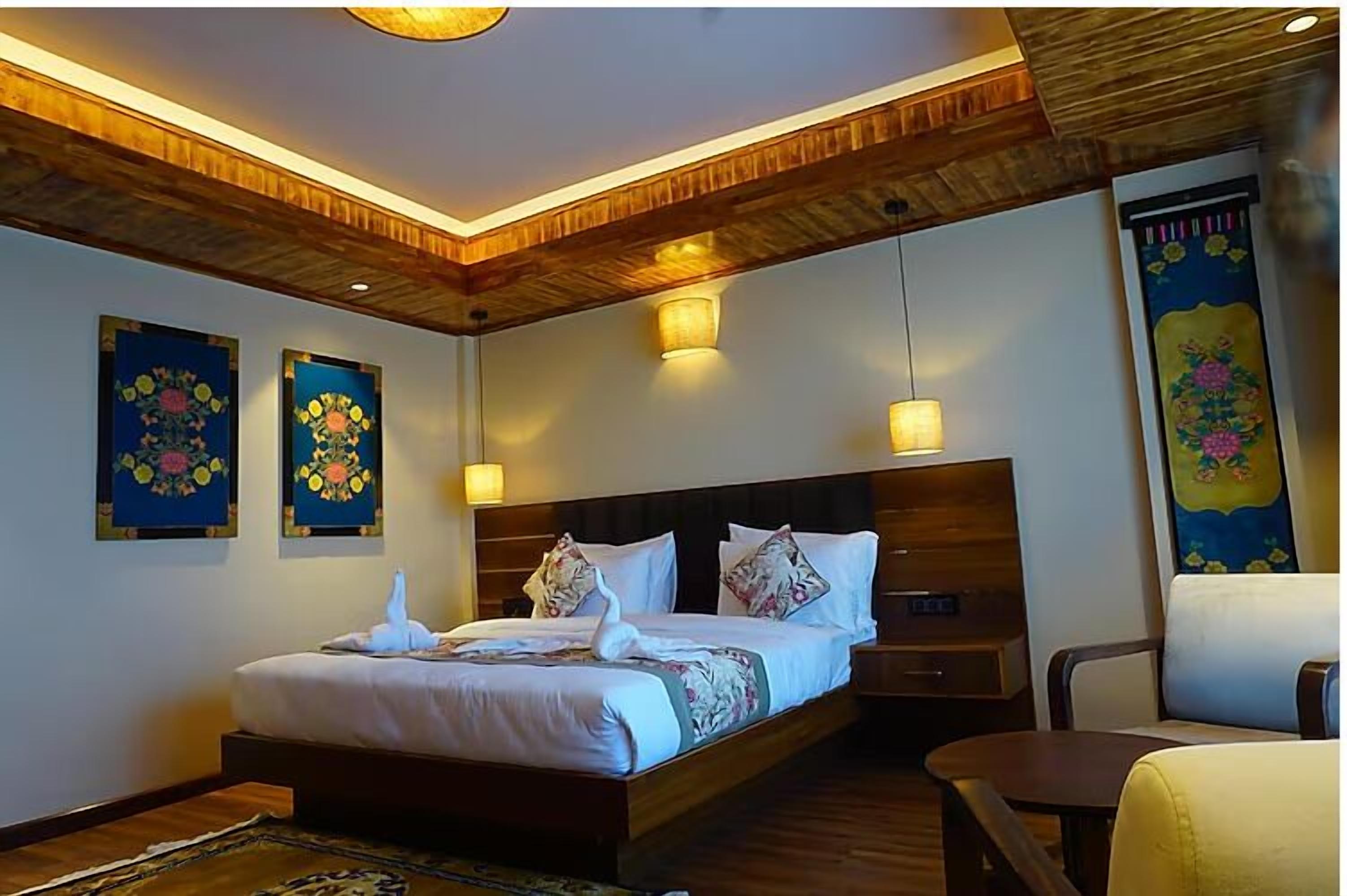 Une chambre d’hôtel avec un plafond en bois, un grand lit avec une literie blanche, deux lampes fixées au mur et deux œuvres d’art florales encadrées.