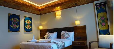 Une chambre d’hôtel avec un plafond en bois, un grand lit avec une literie blanche, deux lampes fixées au mur et deux œuvres d’art florales encadrées.