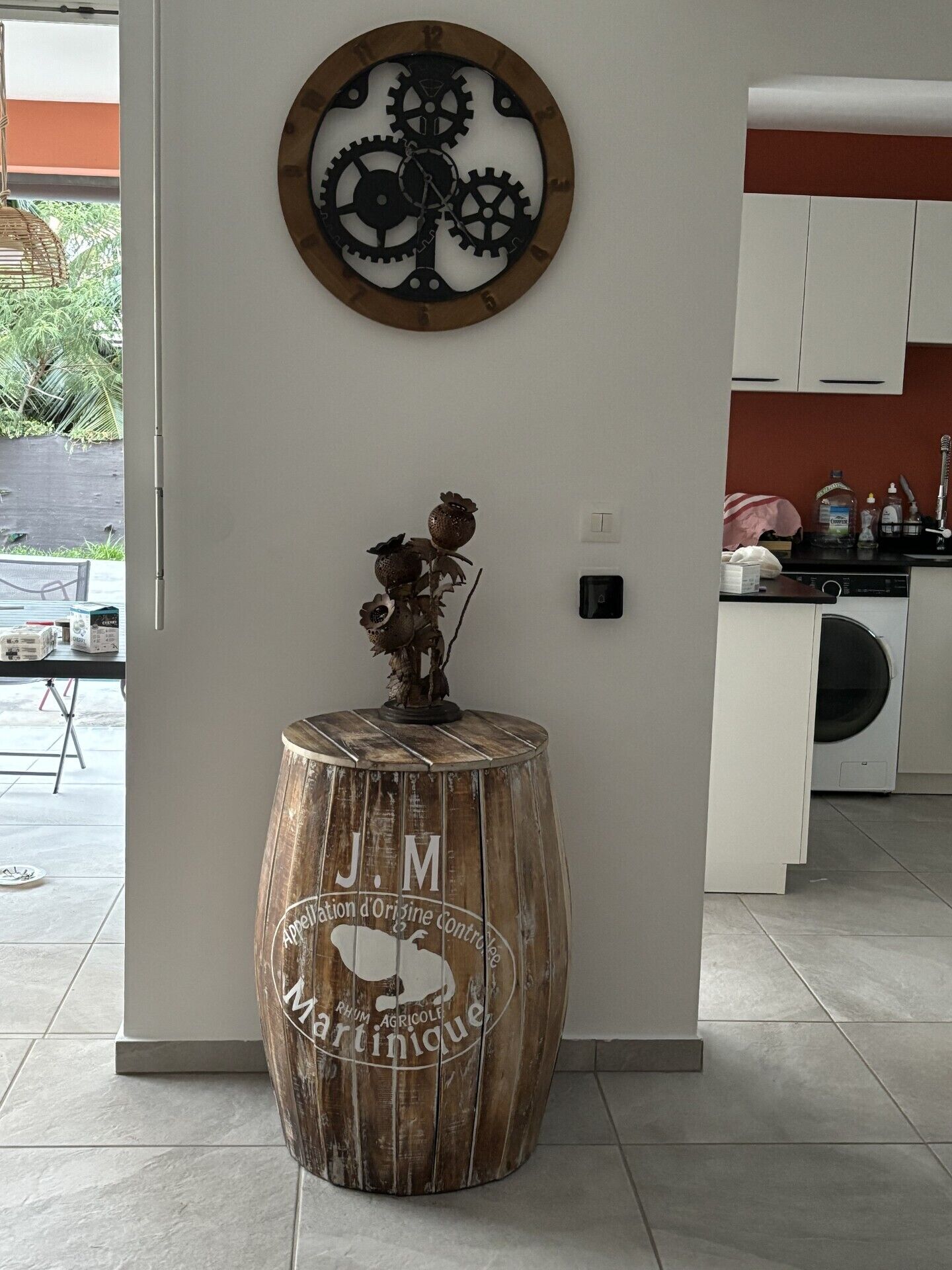 A kitchen with white cabinets, a wooden barrel with branding, a wall clock, and a small plant on a wooden stool.
