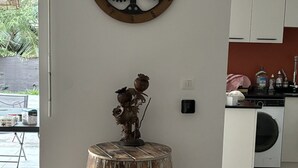 Une cuisine avec des armoires blanches, un tonneau en bois portant une marque, une horloge murale et une petite plante posée sur un tabouret en bois.
