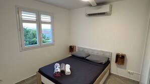 Une chambre avec un lit, un ventilateur de plafond, un appareil de climatisation, une fenêtre et une vue sur la verdure à l’extérieur.