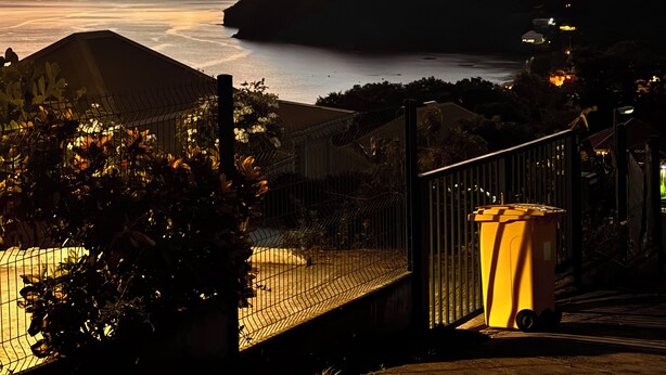 Une vue sur la côte avec un coucher de soleil, une zone délimitée par une clôture et une poubelle.