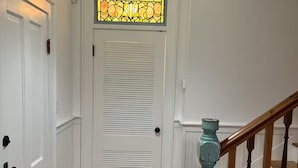 Een hal met houten vloer, witte deuren, een glas-in-loodraam boven een deur, en een houten trap met blauwe accenten.