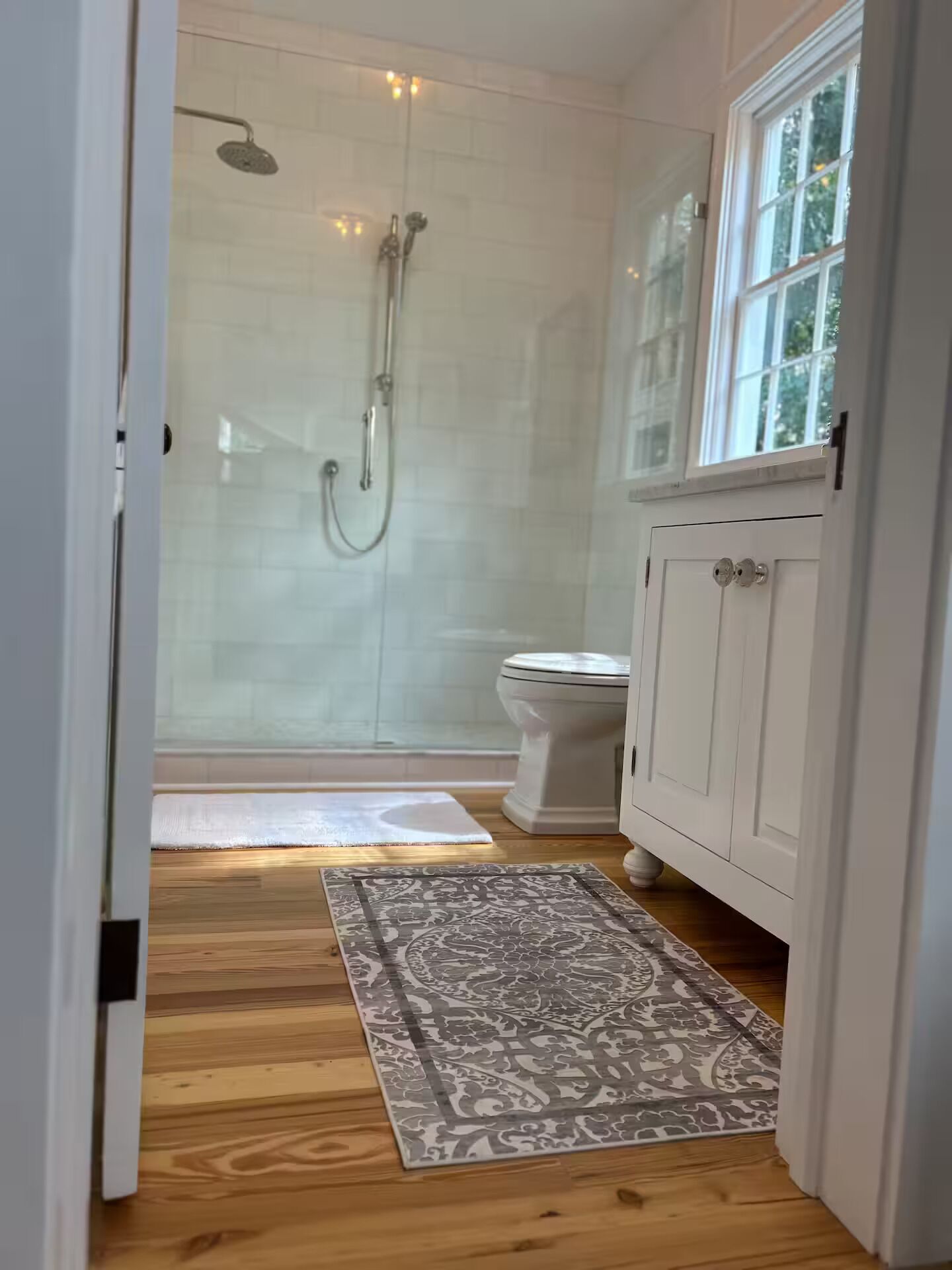 Une salle de bain avec une douche à parois de verre, des toilettes et un plancher en bois.